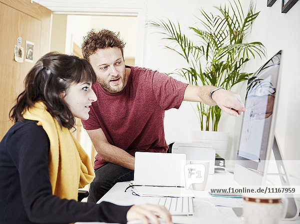 Zwei Menschen arbeiten zusammen in einem Büro und schauen auf einen Computerbildschirm.