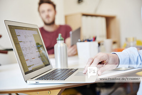 Ein Mann mit einem Laptop und ein Mann mit einem digitalen Tablett  die in einem Büro arbeiten.