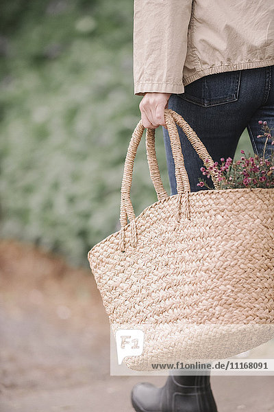 Eine Frau trägt einen Weidenkorb mit Blumen.