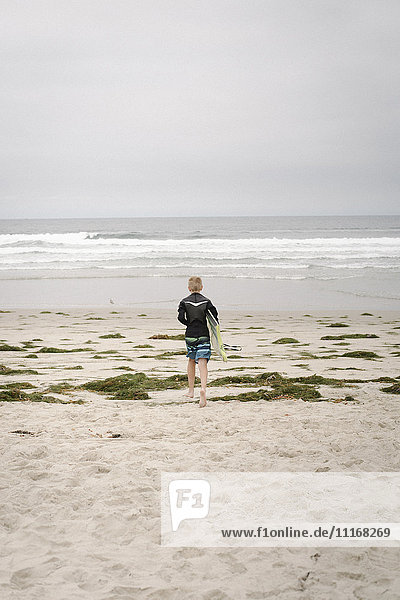 Rückansicht eines Jungen  der ein Bodyboard trägt und in den Ozean geht.