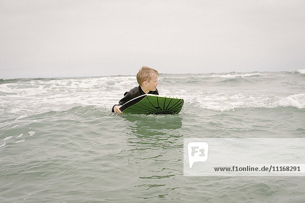 Blonder Junge beim Bodyboarding im Meer.