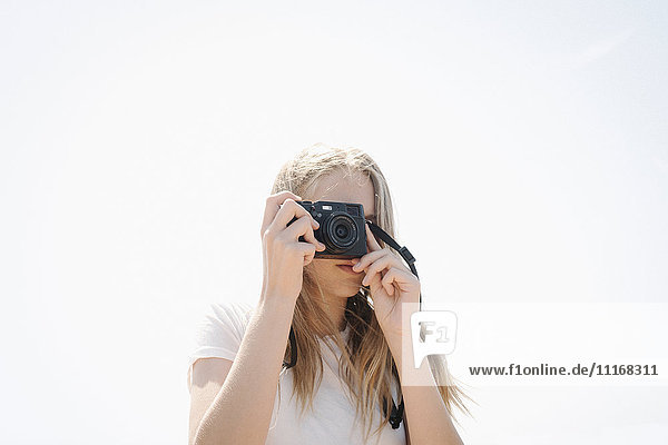 Teenage girl with long blond hair looking through a camera  taking a picture.