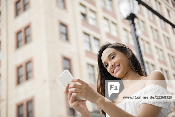 Lächelnde Mixed-Race-Frau  die in der Stadt eine SMS auf ihrem Handy schreibt