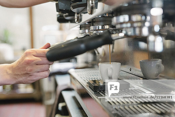 Nahaufnahme eines Mannes  der vor einer Espressomaschine steht  frischer Espresso läuft in eine Tasse.
