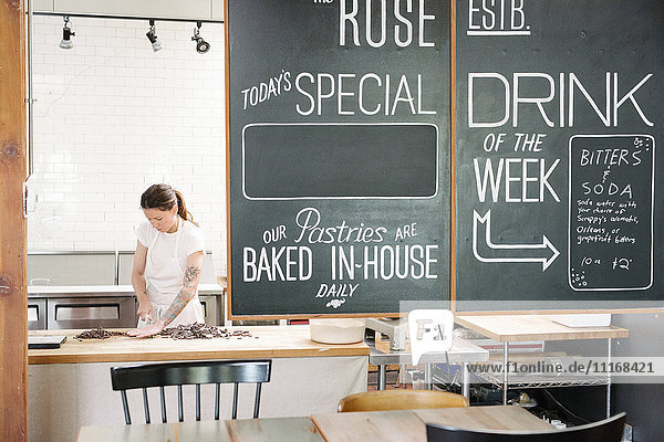 Frau mit weißer Schürze an einem Arbeitstresen in einer Bäckerei  Menü an einer Tafel.