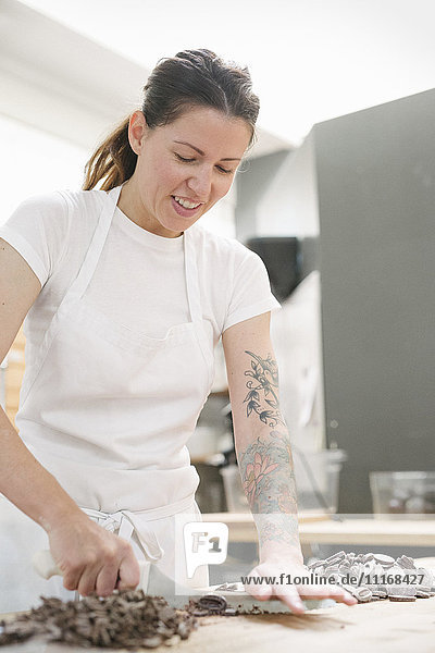 Frau mit weißer Schürze steht an einem Arbeitstresen in einer Bäckerei und hackt Schokolade.