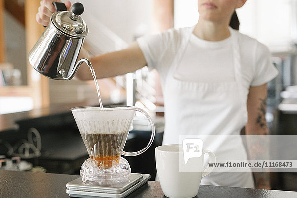 Frau mit weißer Schürze steht in einem Café und macht Filterkaffee.