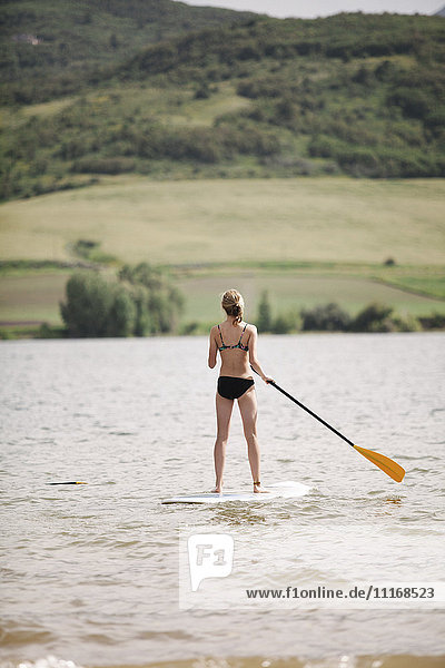 Ein junges Mädchen steht auf und paddelt auf einem See.