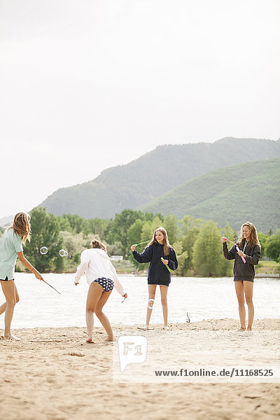 Mädchen im Teenageralter stehen an einem See  umgeben von Seifenblasen.