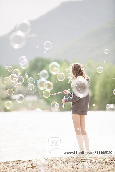 Ein junges Mädchen steht an einem See  umgeben von Seifenblasen.