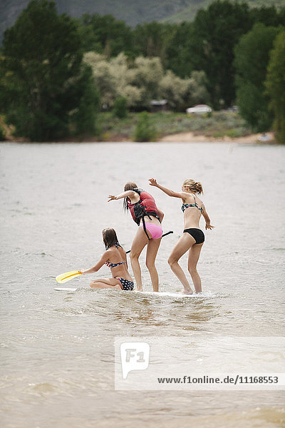 Drei Mädchen im Teenageralter auf einem Paddelbrett auf einem See.