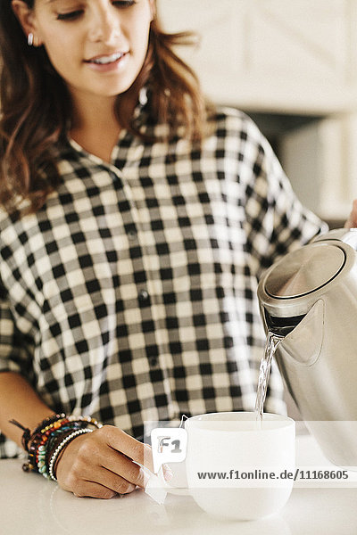 Woman with long brown hair  wearing a chequered shirt  making a cup of tea.