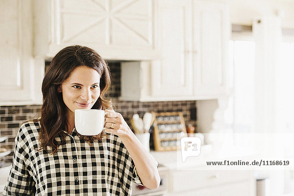 Woman with long brown hair  wearing a chequered shirt  drinking from a mug.