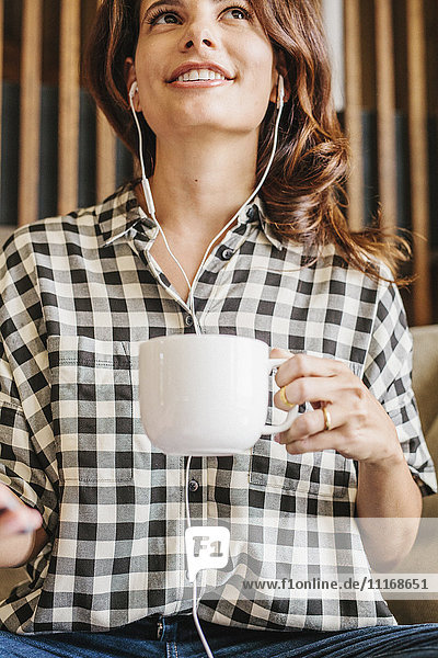 Woman with long brown hair  wearing headphones and chequered shirt  holding a mug.