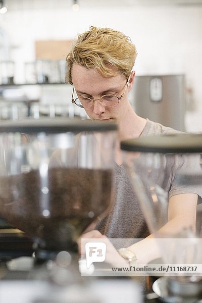 Junger blonder Mann mit Brille  der an einer Espressomaschine in einem Café steht.