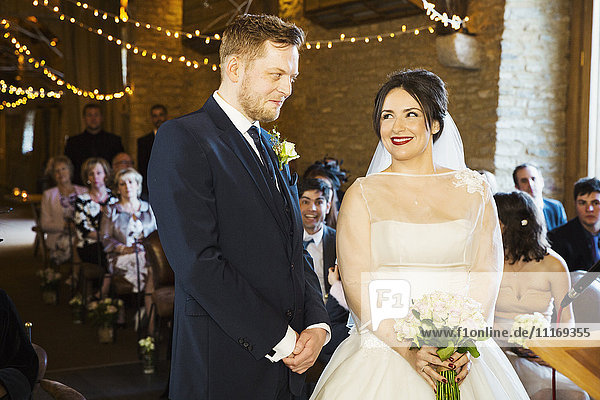 Eine Braut und ein Bräutigam bei ihrer Hochzeitszeremonie  die Seite an Seite vor den Hochzeitsgästen stehen.