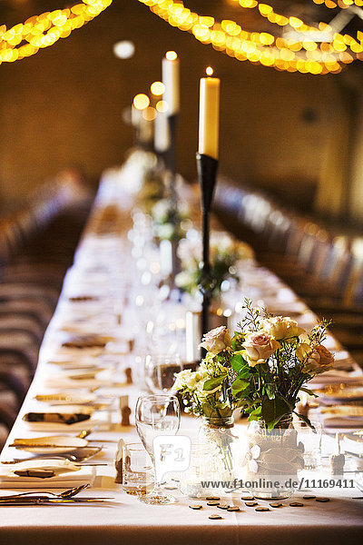 Ein Hochzeitsort  der für eine Party dekoriert ist  mit Lichterketten und einem langen gedeckten Tisch für das Abendessen.