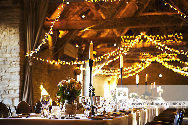 Eine Hochzeitslocation  die für eine Party dekoriert ist  mit Lichterketten und den für das Abendessen gedeckten Tischen.