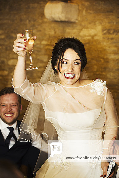 Eine Braut  die an ihrem Hochzeitstag ihr Glas erhebt  um auf die Hochzeitsgesellschaft anzustoßen.