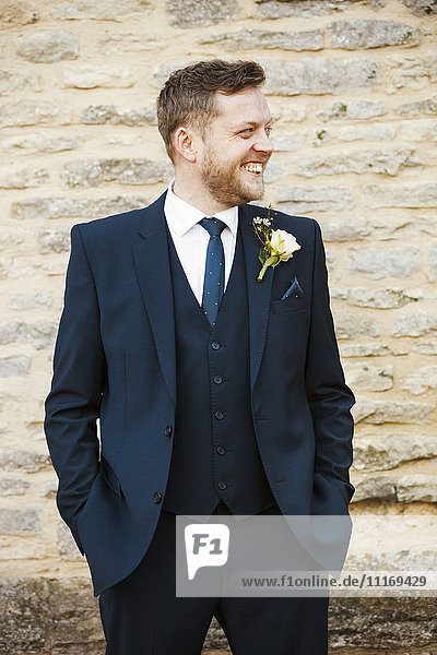 Ein Mann in einem Anzug mit einem Knopfloch  die Hände in den Taschen  lächelnd.