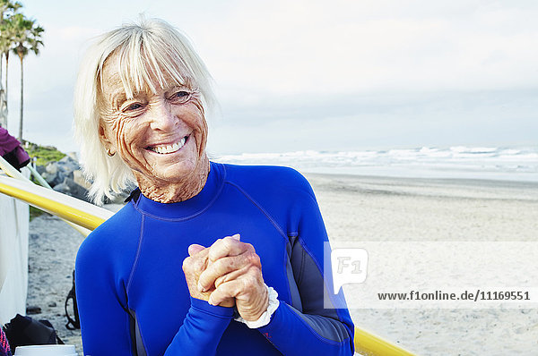 Smiling senior woman wearing a wetsuit  standing on a sandy beach.