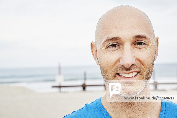 Kahlköpfiger  reifer Mann steht am Strand und lächelt in die Kamera.