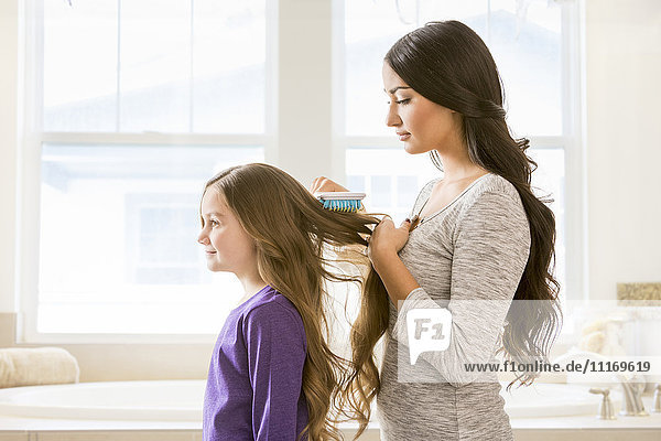 Mother brushing hair of daughter in bathroom