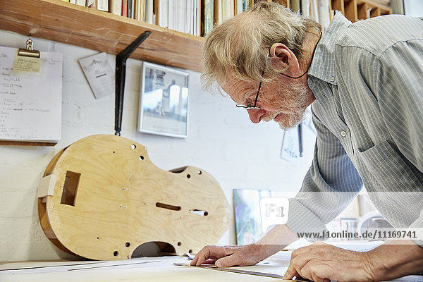 Ein Geigenbauer an seinem Zeichenbrett  der die Pläne und Skizzen für ein neues Instrument entwirft.