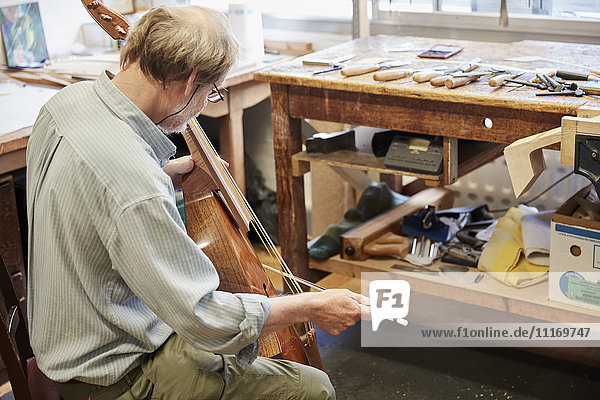 Ein Geigenbauer in seiner Werkstatt  der ein Instrument mit Bogen spielt  stimmte und veredelte.