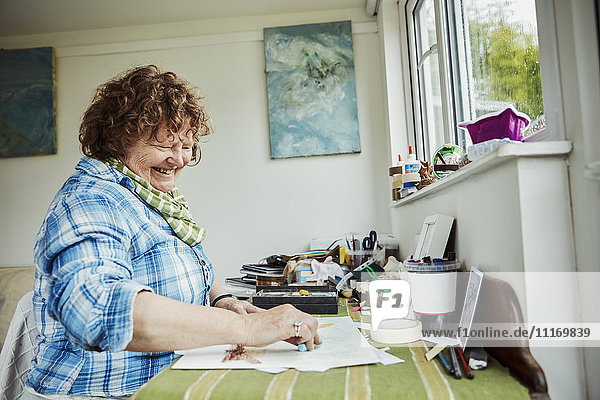 Eine Künstlerin  die an einem Tisch arbeitet  einen großen blauen Pastellstift benutzt und auf Papier zeichnet.