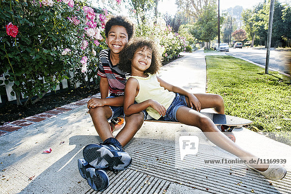 Mixed Race brother and sister sitting on skateboard on sidewalk