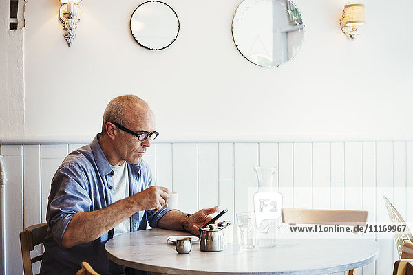 Ein Mann  der an einem Tisch sitzt und sein Smartphone überprüft.