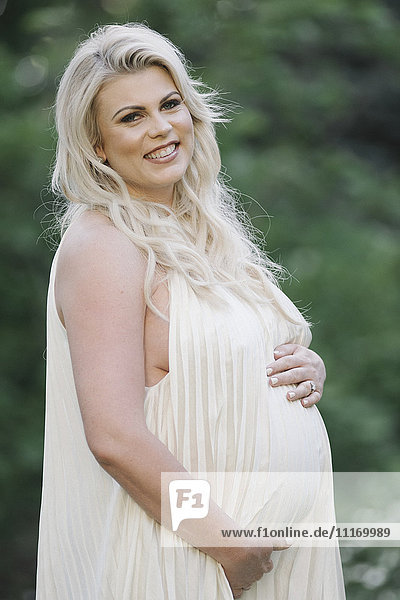 Portrait of a pregnant woman with long blond hair in a garden.
