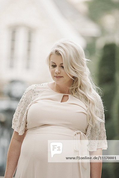 Porträt einer schwangeren Frau mit langen blonden Haaren in einem Garten.