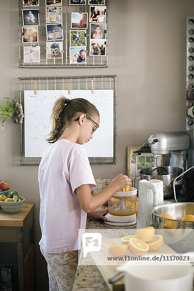 Eine Familie bereitet das Frühstück in einer Küche vor  ein Mädchen quetscht Orangen.