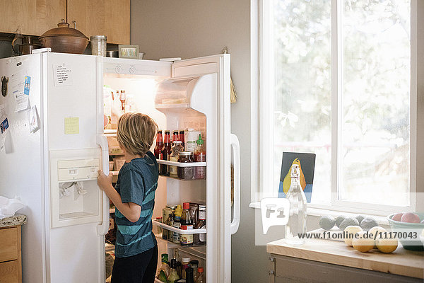 Family preparing breakfast in a kitchen  boy standing at an open fridge.