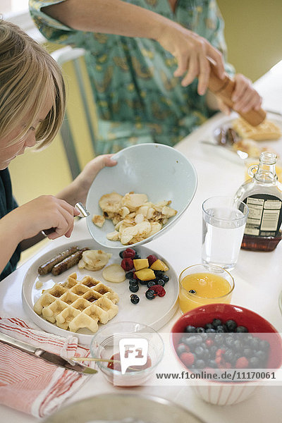 Boy sitting at breakfast table  waffles  fruit and juice.