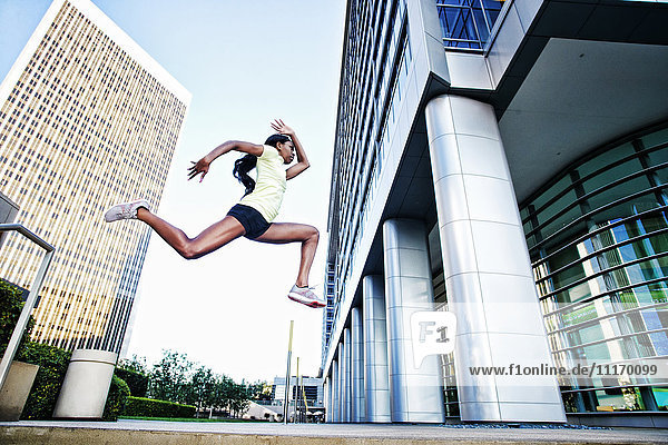 Black woman running and jumping on city sidewalk