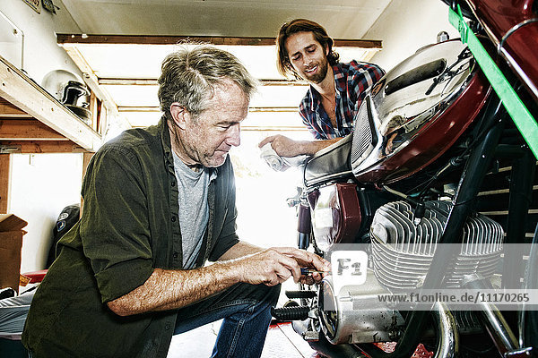 Kaukasischer Sohn beobachtet Vater bei der Reparatur eines Motorrads in der Garage