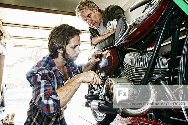 Kaukasischer Vater beobachtet Sohn bei der Reparatur eines Motorrads in der Garage