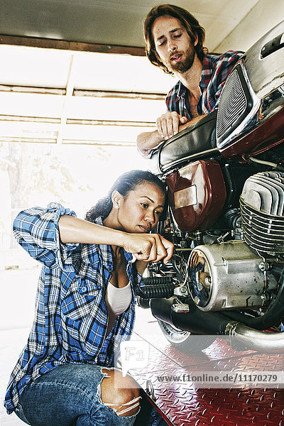Mann beobachtet Frau bei der Reparatur eines Motorrads in der Garage