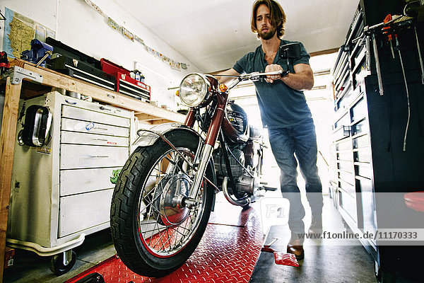 Kaukasischer Mann  der ein Motorrad auf einem Reparaturstand in einer Garage schiebt