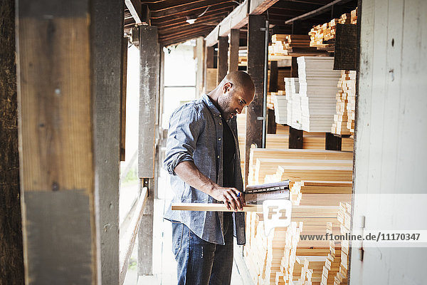 Man standing in a lumber yard  holding a folder  checking wood.