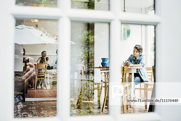 Blick durch ein Fenster in ein Cafe  Menschen sitzen an Tischen.