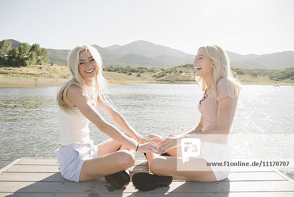 Porträt von zwei blonden Schwestern  die auf einem Steg sitzen.