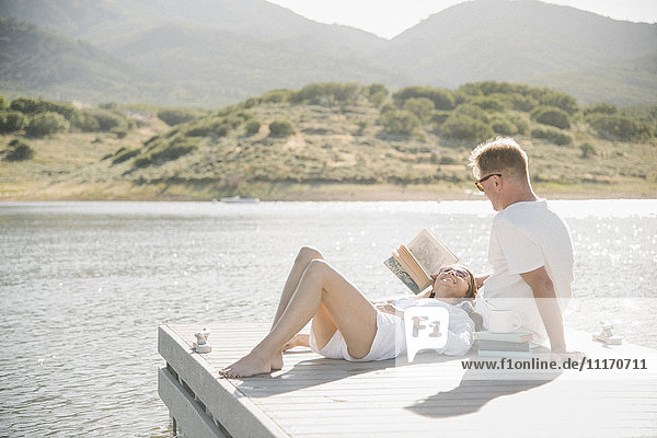 Man and woman reclining on a jetty  reading a book.