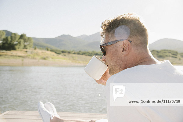 Man sitting on a jetty  drinking from a mug.