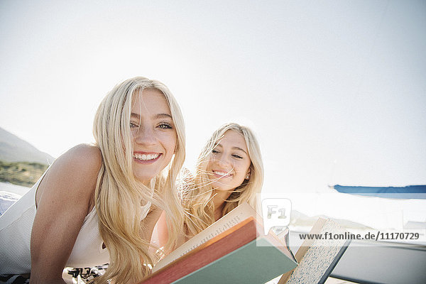 Two blond sisters lying on a jetty  reading a book.