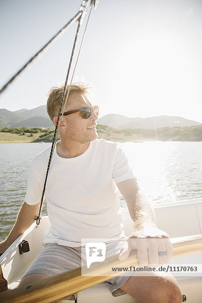 Portrait of a blond man with sunglasses steering a sail boat.
