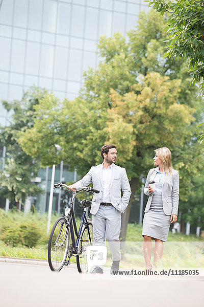 Businesspeople with bicycle conversing while walking on street